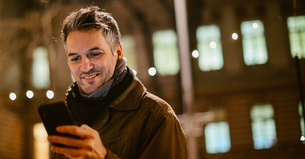 A man outside on a cold night looking at his phone.